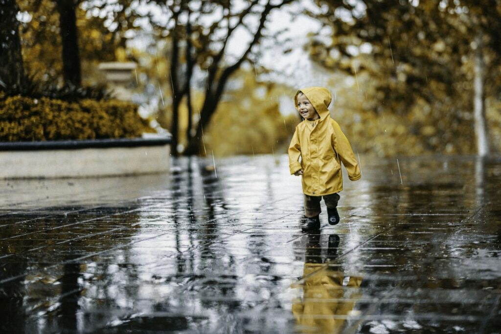 Enfant en imperméable jaune marchant sous la pluie dans un parc en automne